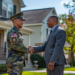 Photo of a Realtor in a business suit shaking hands with a US military officer, with a suburban house in the background on a sunny day